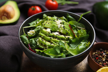 Bowl of tasty avocado salad with mozzarella cheese and peppercorns on wooden background, closeup