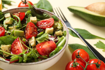 Bowl of tasty avocado salad with cherry tomatoes on yellow background, closeup