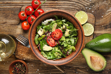 Bowl of tasty avocado salad with cherry tomatoes and lime on wooden background