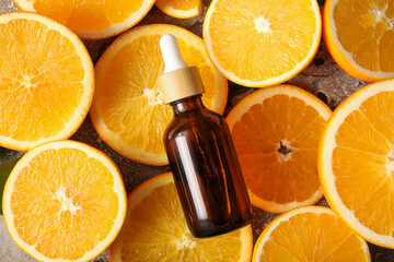 Bottle of orange essential oil and slices of fresh fruit on grey background