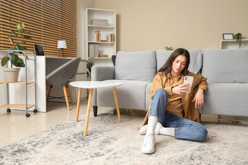 Portrait of worried young woman with mobile phone at home