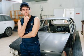 Portrait of pensive mechanic male in jumpsuit serious looking at camera not knowing what disrepair during maintenance car in repair workshop. Doubtful repairman trying to solve problem in garage