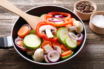 Frying pan with mix of fresh vegetables, mushrooms and spices on wooden table, closeup