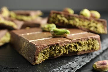 Pieces of Dubai chocolate bar with pistachios and knafeh on grey table, closeup