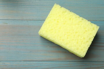 Yellow sponge on light blue wooden table, top view. Space for text