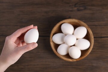 Woman holding raw egg over wooden table, top view
