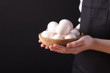 Woman with bowl of raw eggs on black background, closeup. Space for text