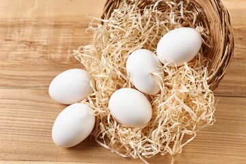 Basket with raw eggs on wooden table, closeup