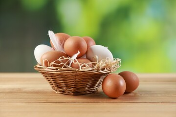 Many raw eggs in basket on wooden table, closeup