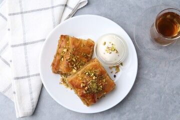 Tasty baklava with chopped nuts, scoop of ice cream and tea on grey table, top view