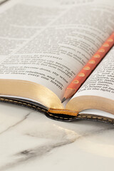 Open holy bible book with pencil on white marble table. Close-up. Selective focus. Christian education, studying Scriptures, biblical concept.
