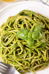 Vegan spaghetti in green pasta sauce with basil and parmesan cheese in a dish with fork. Top view. Close-up. Healthy homemade comfort food concept.