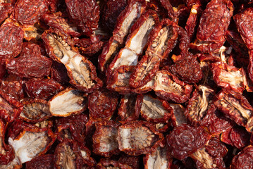 Dried tomatoes are laid out flat next to each other and on top of each other. Some of the tomatoes still have salt on them. The tomatoes are cut open.