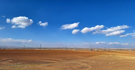 Blue sky with scattered cotton clouds over a dirt field