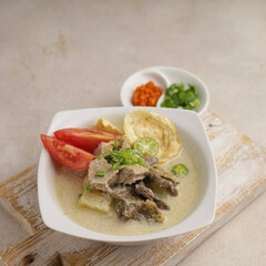 a bowl of Indonesian cuisine or Soto Betawi, a creamy soup served with sliced meat, vegetables and crackers, in white bowl