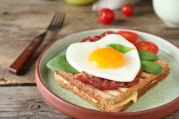 Plate of tasty sandwich with heart shaped fried egg and  bacon on wooden table, closeup