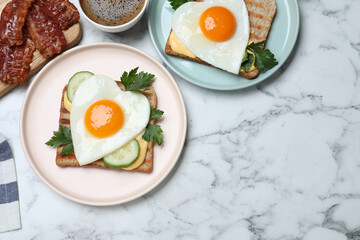 Tasty sandwiches with heart shaped fried eggs for romantic breakfast on white marble table, flat lay. Space for text