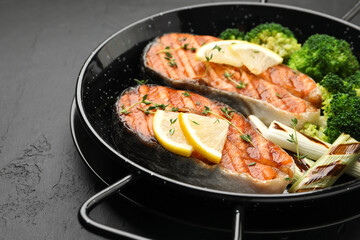 Tasty grilled salmon steak with lemon and vegetables on dark textured table, closeup