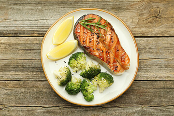 Tasty grilled salmon steak, broccoli, lemon and rosemary on wooden table, top view