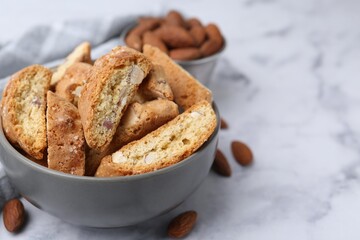 Tasty almond biscuits (Cantuccini) in bowl and nuts on light marble table, closeup. Space for text