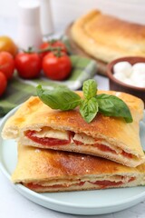 Pieces of tasty vegetarian calzone with tomato, cheese and basil on table, closeup
