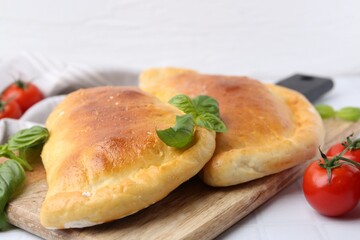 Tasty vegetarian calzones with basil and tomatoes on white table, closeup
