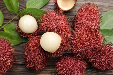 Delicious ripe rambutans and green leaves on wooden table, flat lay