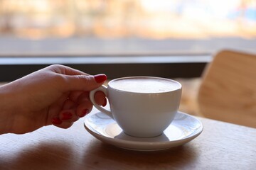 Woman with cup of aromatic coffee at wooden table in cafe, closeup