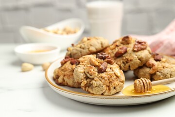 Tasty cookies with nuts and honey dipper on white table, closeup