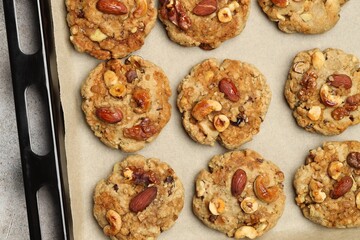 Tasty cookies with nuts in baking tray on gray textured table, top view