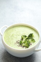 Delicious broccoli cream soup in bowl on light table, closeup