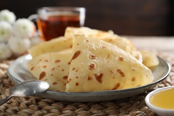 Delicious crepes, honey and spoon on table, closeup