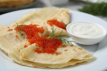 Tasty crepes with red caviar, dill and sauce on plate, closeup