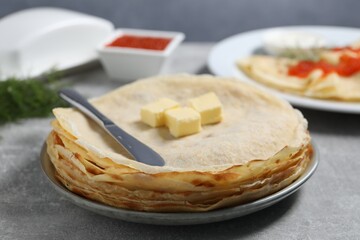 Stack of tasty crepes with butter on grey textured table, closeup