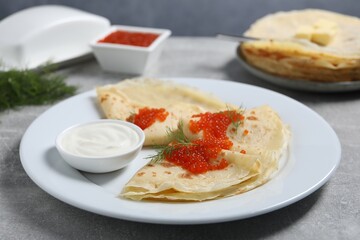 Tasty crepes with red caviar, dill and sauce on grey textured table, closeup
