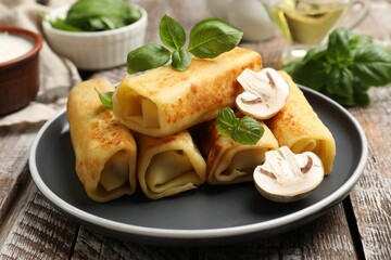 Delicious rolled crepes with mushrooms and basil on wooden table, closeup