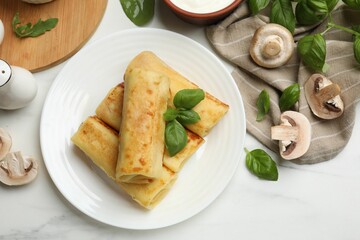 Delicious rolled crepes with mushrooms and basil on white marble table, flat lay
