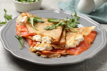 Delicious crepes with salmon, cream cheese and arugula on grey table, closeup