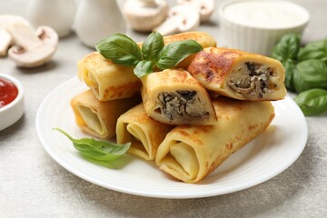 Delicious rolled crepes with mushrooms and basil on grey table, closeup