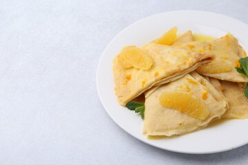 Plate with tasty crepes Suzette on light textured table, closeup. Space for text