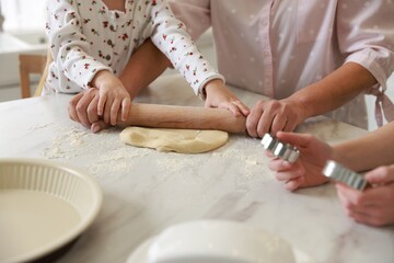 Grandmother and her grandchildren shaping dough with rolling pin at white marble table in kitchen, closeup