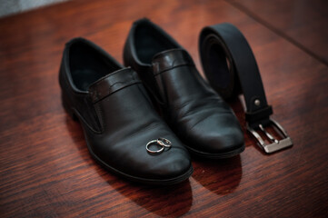 Classic Black Shoes with Wedding Rings and a Belt on a Wooden Surface
