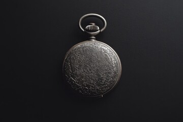 An antique silver pocket watch with a textured surface rests on a dark background.