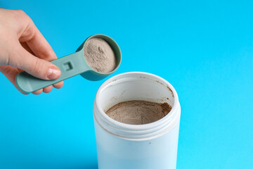 Woman taking scoop of protein from jar on light blue background, closeup