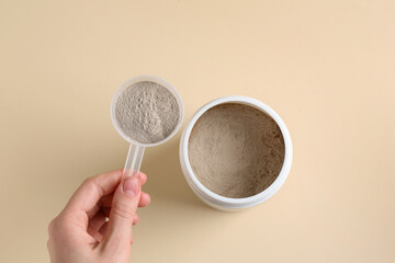 Woman taking scoop of protein from jar on beige background, top view