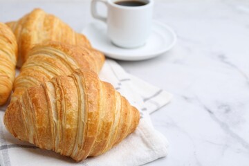 Tasty fresh croissants and cup of coffee on white marble table, closeup. Space for text