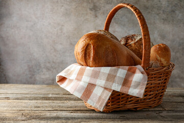 Different freshly baked bread loafs in wicker basket on wooden table, space for text