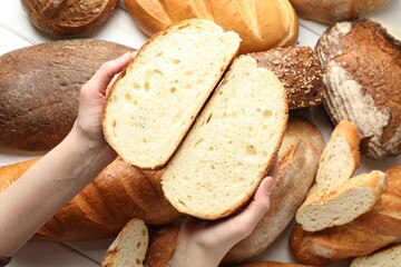 Woman with pieces of fresh bread over different other loafs at white table, top view