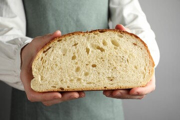 Woman with piece of fresh bread on grey background, closeup