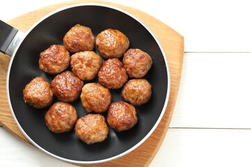 Tasty meatballs in frying pan on white wooden table, top view. Space for text